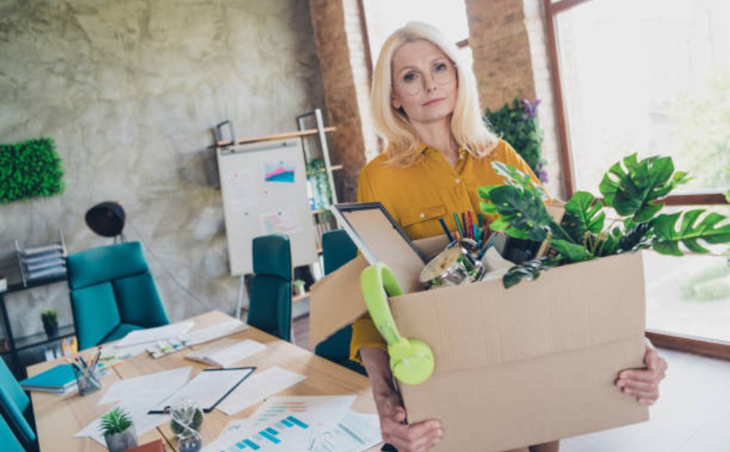 Fired office worker leaving workstation with a box