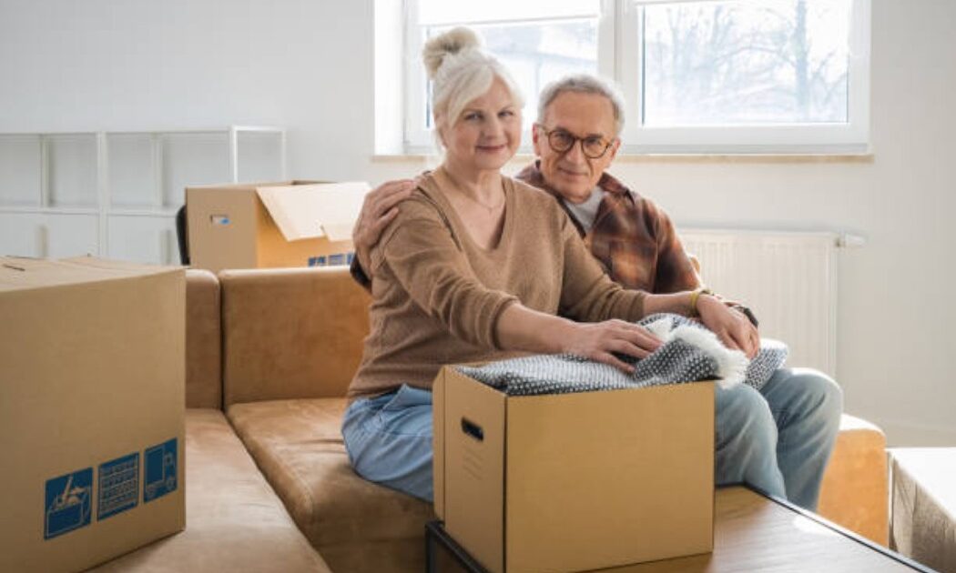 Senior couple stepping up the porch with moving boxes and bright smiles