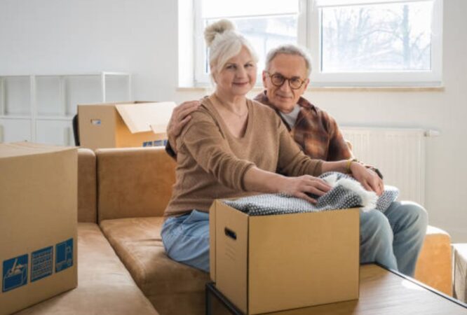 Senior couple stepping up the porch with moving boxes and bright smiles