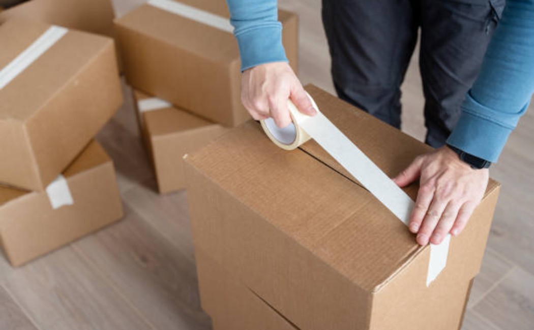 A man using adhesive tape to seal a cardboard box for moving.